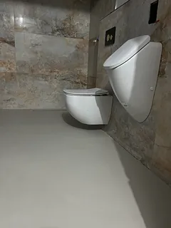 Gäste-WC mit fugenlosem hellem Boden, wandhängendem WC und Urinal vor Wandfliesen in Steinoptik