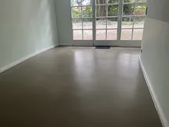 Leerer Wohnraum mit fugenlosem, graubraunem Boden, weißen Sockelleisten und Sprossenfenstern zum Garten